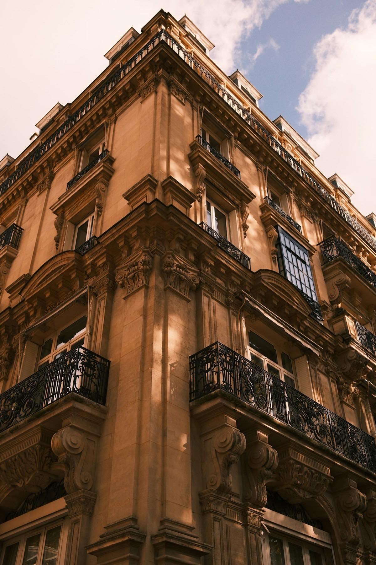 Angle d&rsquo;un immeuble haussmannien dans une lumi&egrave;re dor&eacute;e, balcons en fer forg&eacute;.