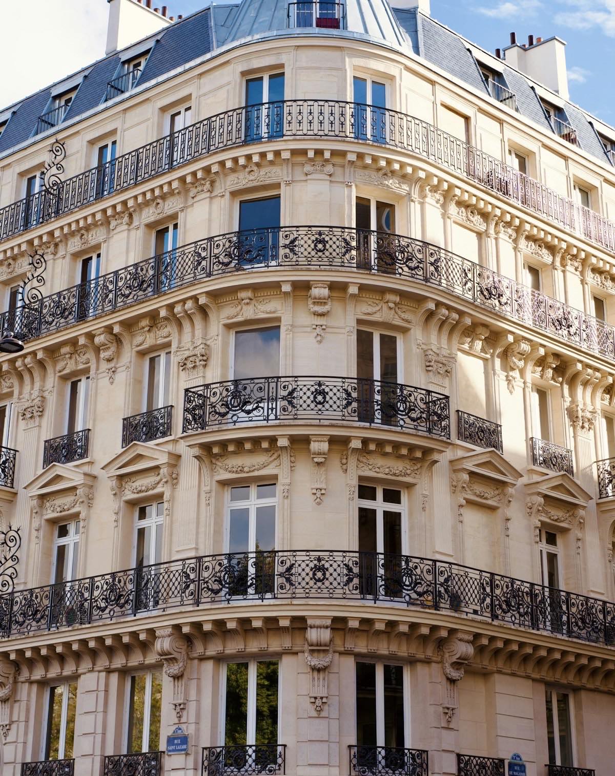 Angle arrondi d&rsquo;un immeuble haussmannien, balcons ouvrag&eacute;s en fer forg&eacute;.